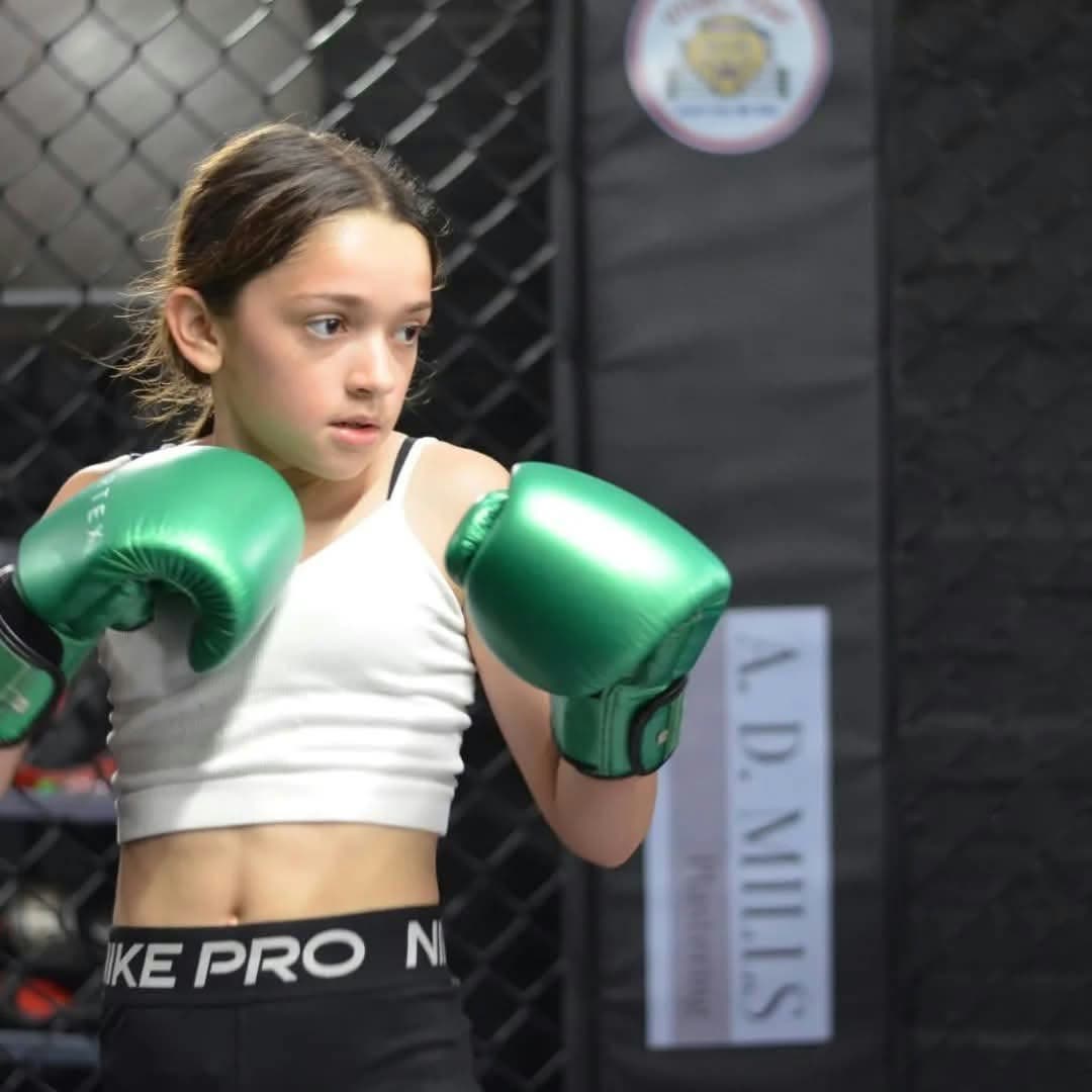 Young girl training in the cage in green boxing gloves