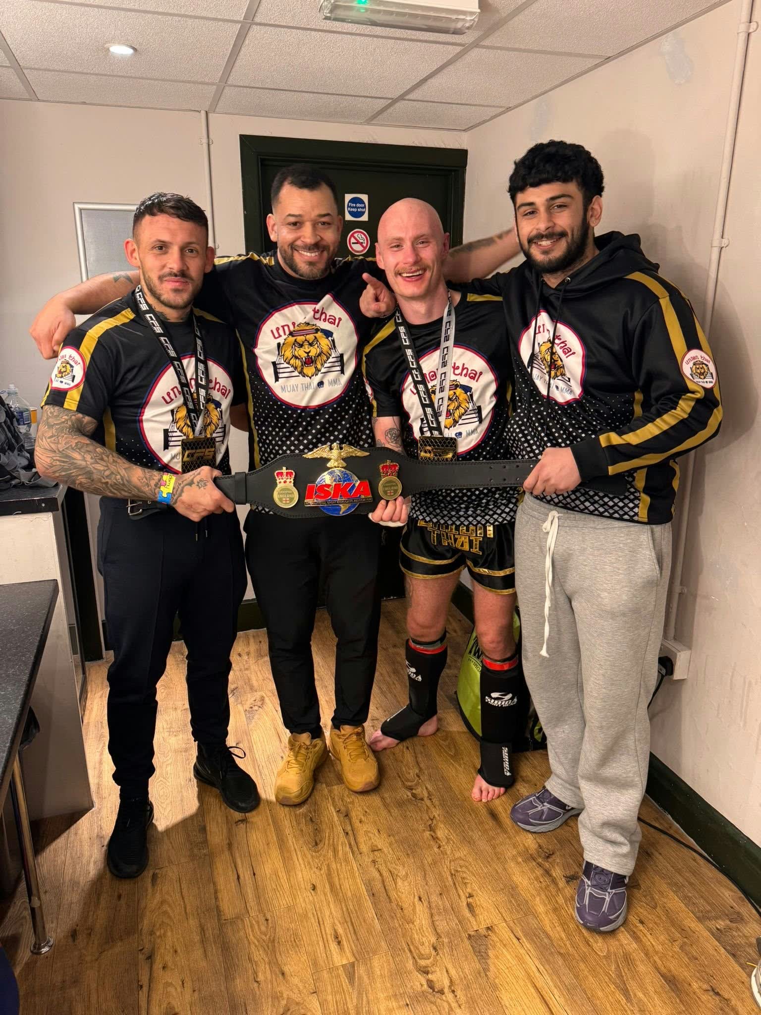 Four Union Thai team members in team shirts holding an ISKA championship belt